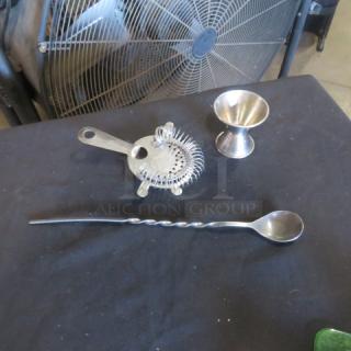 Stainless steel bar accessories set with cocktail strainer, jigger, and twisted mixing spoon on display.