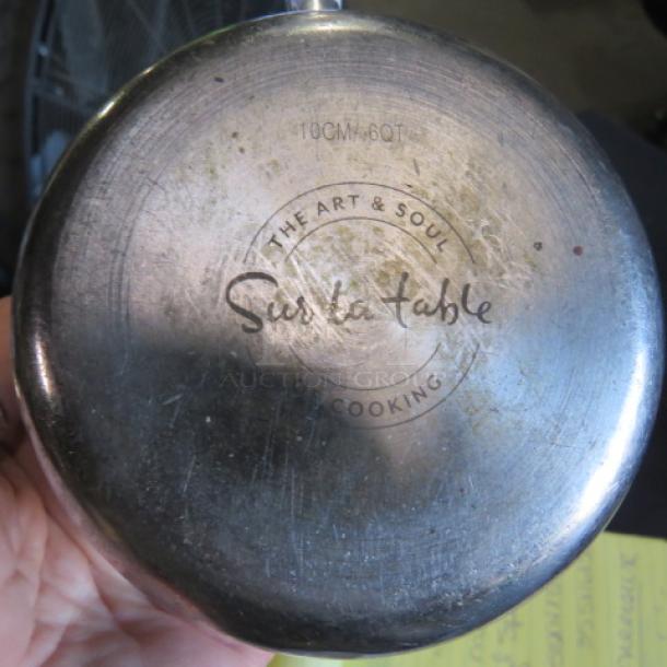 Stainless steel Sir La Table saucepan, bottom view with "The Art & Soul of Cooking" logo and "10CM-60T" marking, used condition.