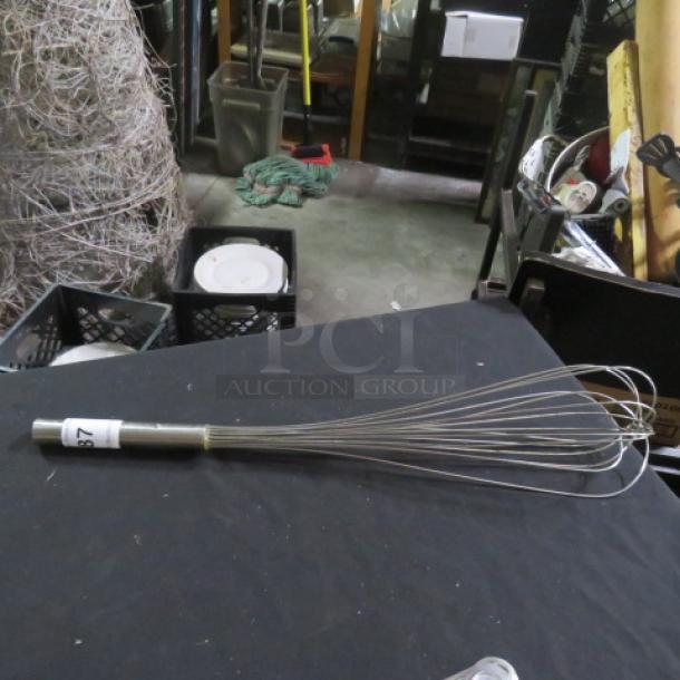 Stainless steel whip with multiple wires, used condition, visible label marked "87", sturdy handle, ideal for mixing.