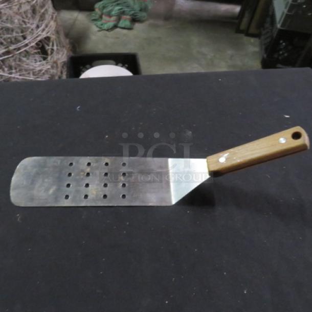 Stainless steel hamburger turner with a wooden handle and perforated blade, in used condition.