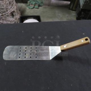 Stainless steel hamburger turner with a wooden handle and perforated blade, in used condition.