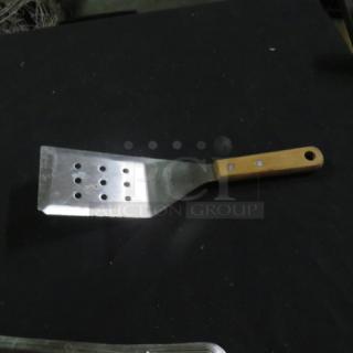 Metal hamburger turner with a wooden handle and perforated blade, sturdy build, shows minor wear, suitable for grilling tasks.