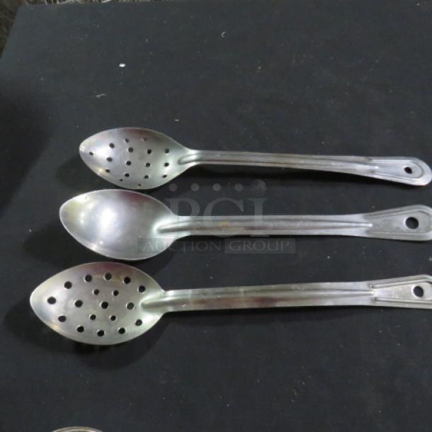 Three assorted stainless steel spoons, two slotted and one solid, in good condition on a black surface.