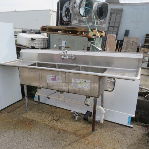Stainless steel three-compartment sink with faucet, 90x24x45, industrial design, mounted on legs, visible wear, labels attached.