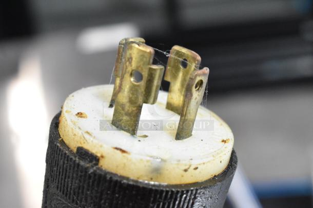 Close-up of a metal electrical plug with three brass prongs, showing signs of wear.