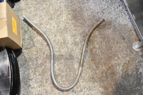 A metal hose on a concrete floor, next to a cardboard box labeled "Grainger Part #4WCA6".