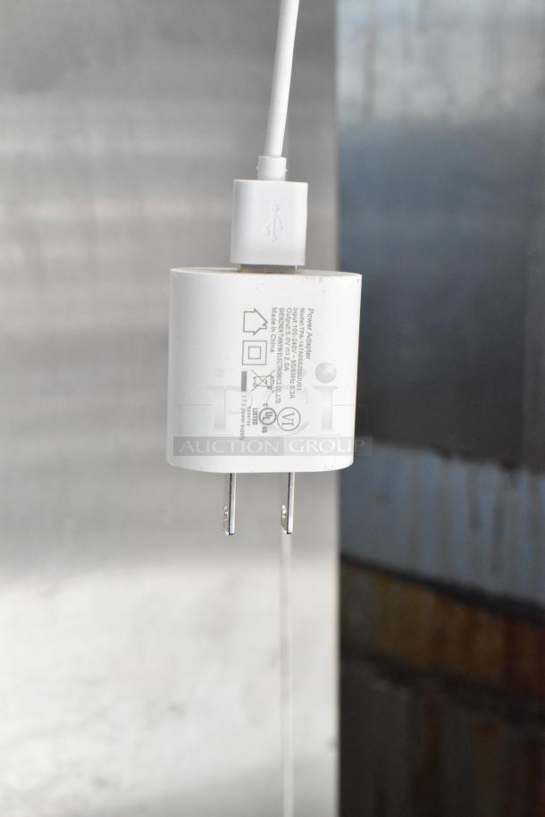 White plug-in power adapter with USB port, showing electrical specifications and certification labels.