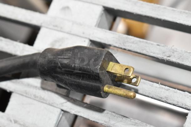 Close-up of a black three-prong plug, part of the JBT Fresh N Squeeze POS-1 citrus juicer, resting on a metallic surface.