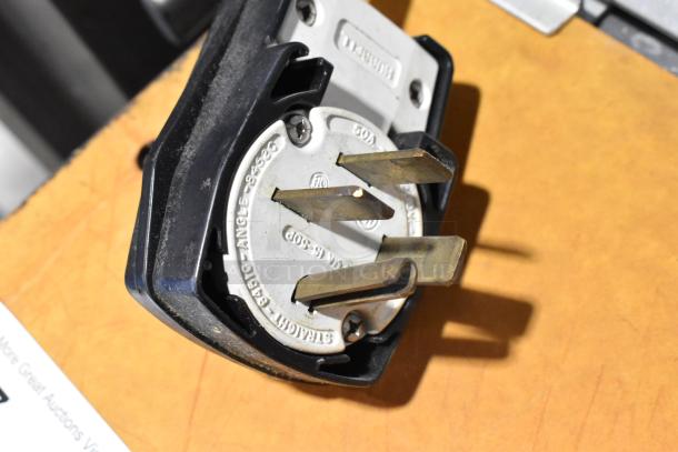 Close-up of a heavy-duty plug for Fri-jado STG7-P rotisserie oven, showing three brass prongs and a branded metal base.