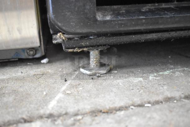 Close-up view of a leveling foot under an IDW G-10-F334B-HC cooler. Shows wear and dust on the metal surface.