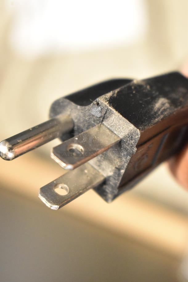 Close-up of a plug from the Curtis D1000GT63A000 coffee machine, showing three metal prongs and slight wear.