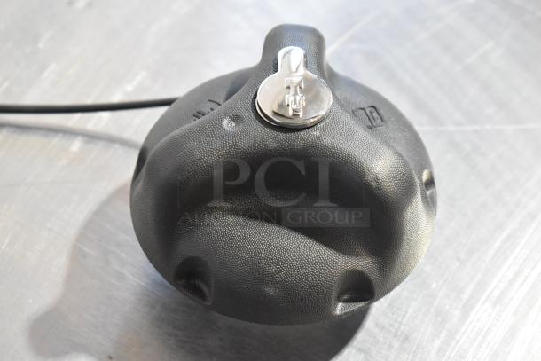 Black cap with a silver lock mechanism, textured surface. Cable attached, ideal for securing items. Condition: new.