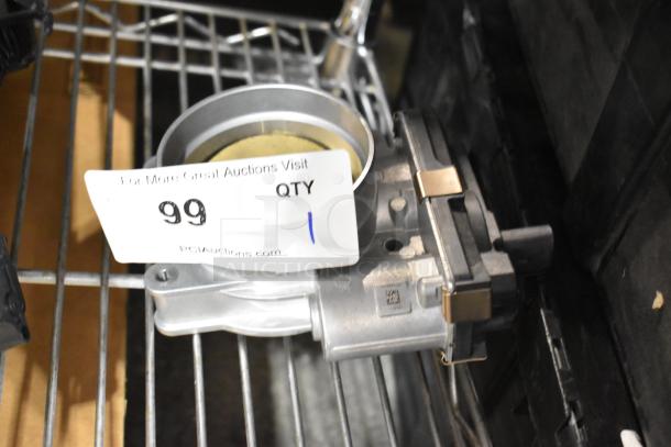Metal unit on a shelf with tag labeled "99 QTY," indicating quantity. Metallic components with visible screws and connectors.