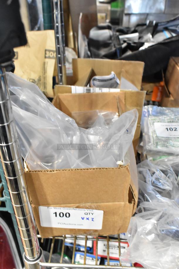 Cardboard box containing GM metal part with plastic wrapping; auction label reads "100 QTY VXZ" for bulk purchase.