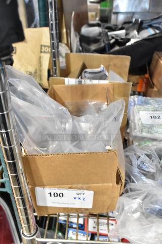 Cardboard box containing GM metal part with plastic wrapping; auction label reads "100 QTY VXZ" for bulk purchase.