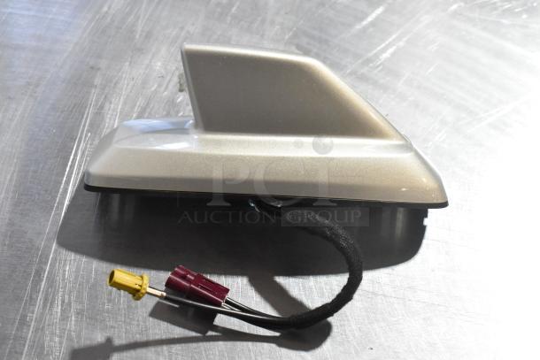 Silver shark fin car antenna with attached cables, set on a metallic surface.