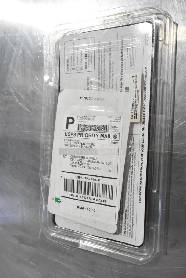 Plastic-wrapped package containing a vent and license plate frame, featuring USPS priority mail labels and tracking info.