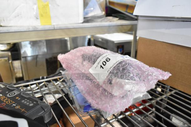 4 items including GM wheel locks and A/C heat panel, bubble-wrapped, labeled "106" by PCIAuctions.com, on metal shelf.