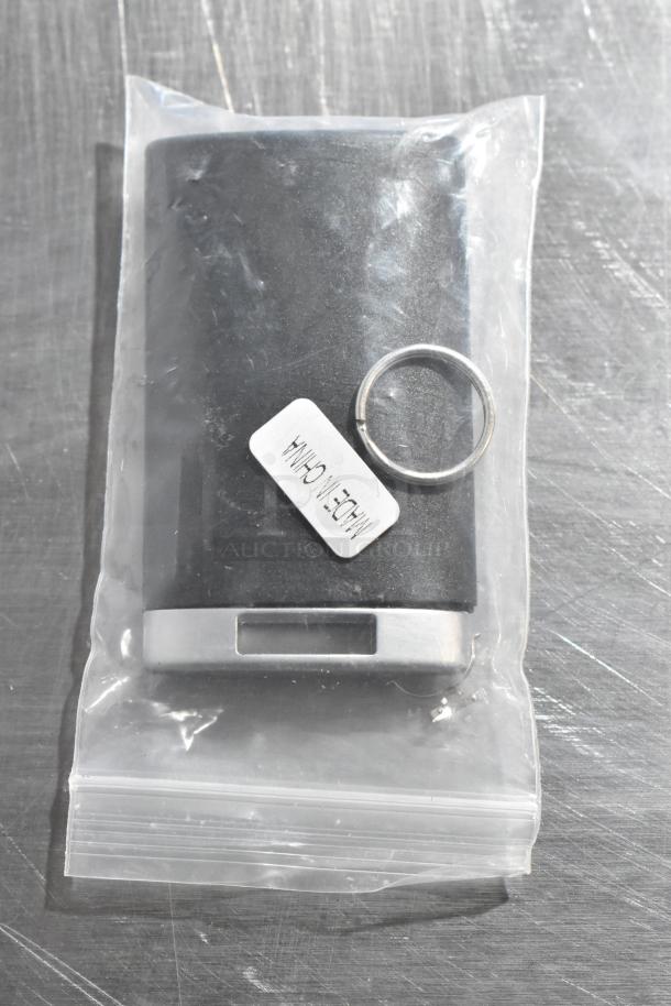 Sealed black and silver device in plastic bag with "Made in China" label and keyring on metal surface.