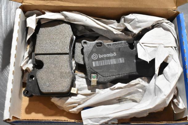 Box containing Brembo brake pads, featuring a label with logo and barcode. Items wrapped in protective paper.