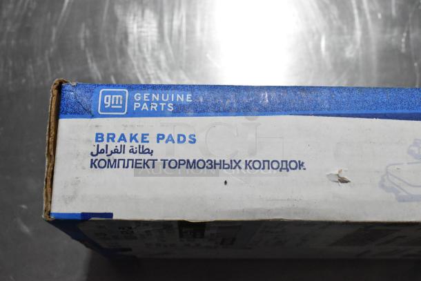 GM Genuine Parts brake pads box with multilingual labeling, part of auction lot including NGK bulb and Hawk pads. Dusty exterior.