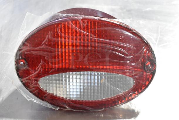 Red and clear oval brake light piece, possibly GM, in protective wrap on a metallic surface.
