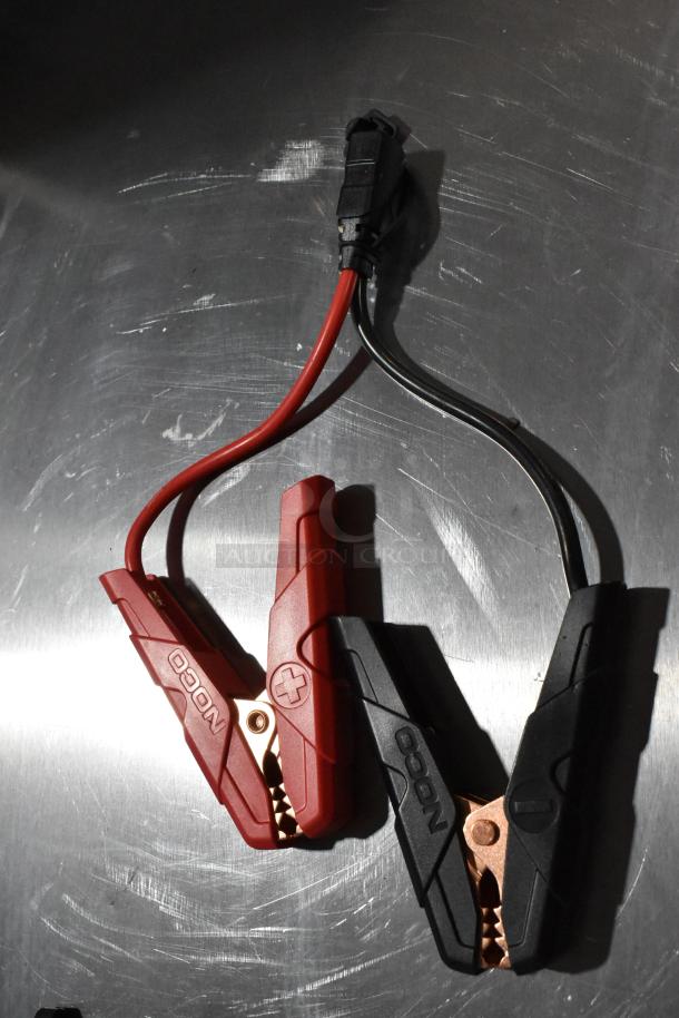 Noco GB40 Genius Boost jumper cables, red and black clamps, shown on a metallic surface, in new condition.