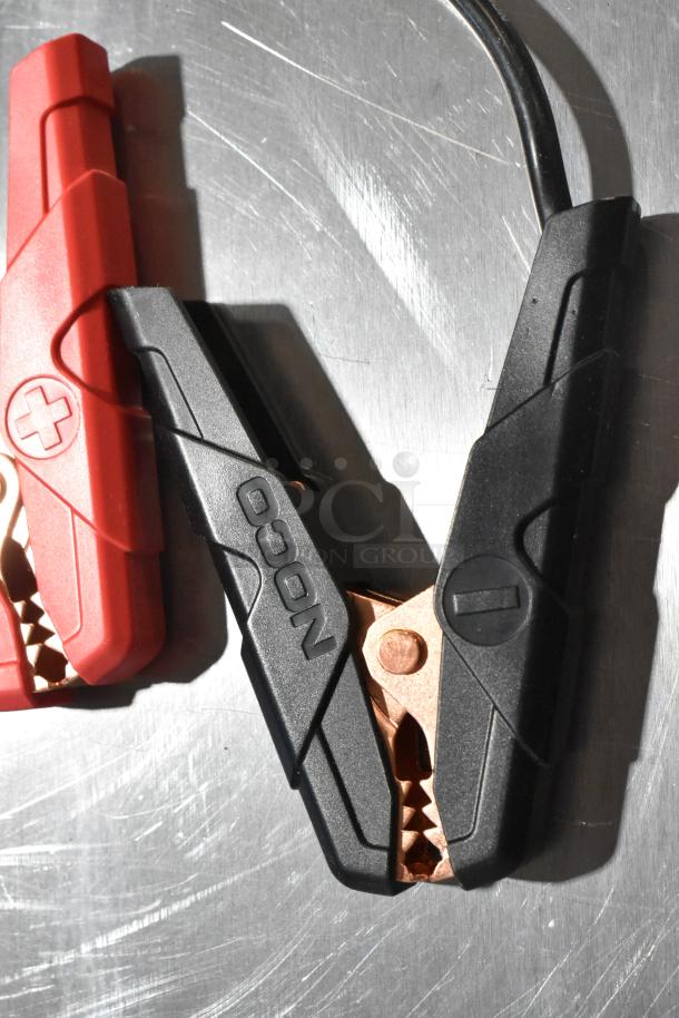 Two clamps of Noco GB40 Genius Boost in red and black with visible "+" and "-" symbols on a metallic surface.