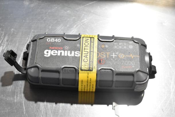 Noco GB40 Genius Boost, 12V 1000A jump starter with caution label, shown on metal surface.