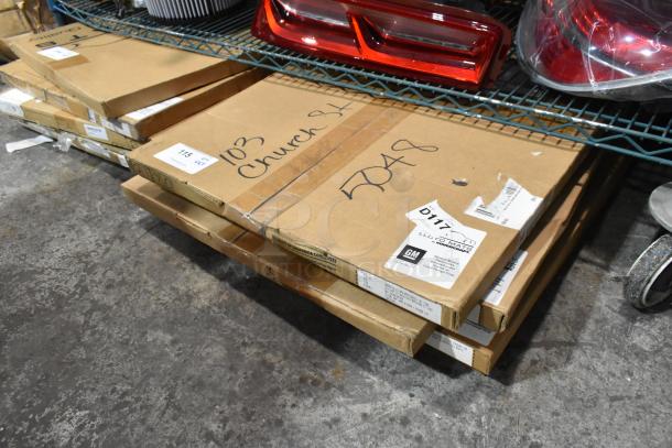 Five new boxed items on wire rack, including Corvette and Silverado floor mats. Boxes show GM labels and scratch markings.