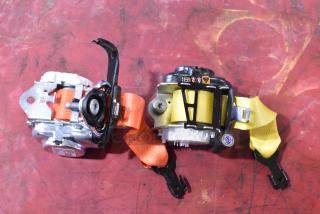 Two seat belt retractors with orange and yellow straps on a red surface, featuring safety icons and mounting brackets.