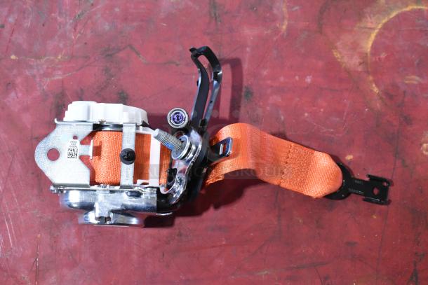 Orange seat belt mechanism on a red background, featuring metallic components and stitching. Includes QR code and markings.