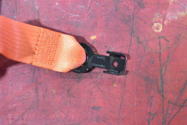 Orange seat belt with metal fastener on red surface, marked "Z10B94" and "Z82A0882A." In good condition.