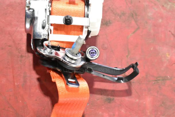 Orange seat belt mechanism with metal components, new condition, suitable for vehicle safety systems.