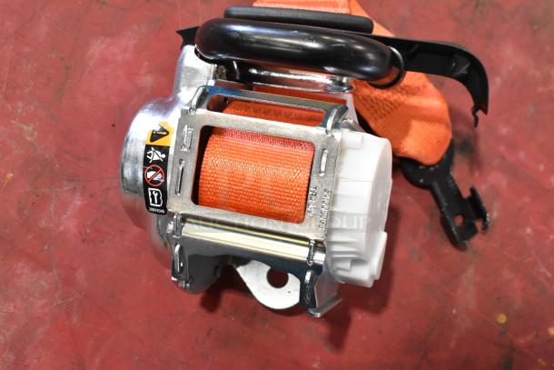 Orange seat belt with sturdy metal and plastic components, featuring safety labels. New condition. Auction includes two items.