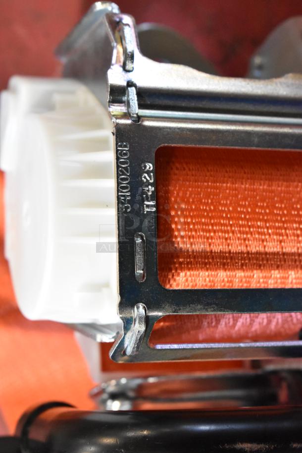 Close-up of a seat belt mechanism with orange webbing and metal frame. Visible markings include "3400206B" and "TF-29".