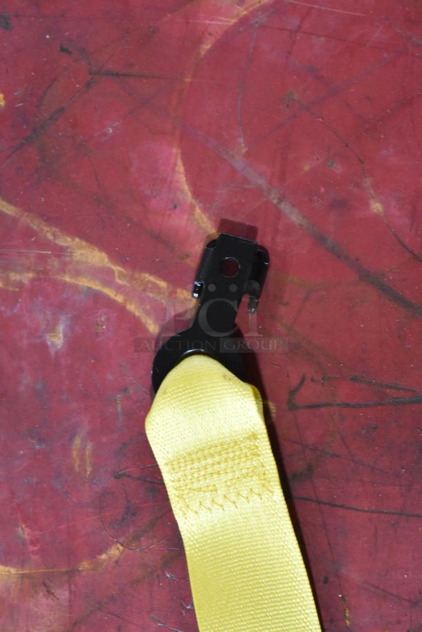 Yellow seat belt with black metal clasp on a red surface.