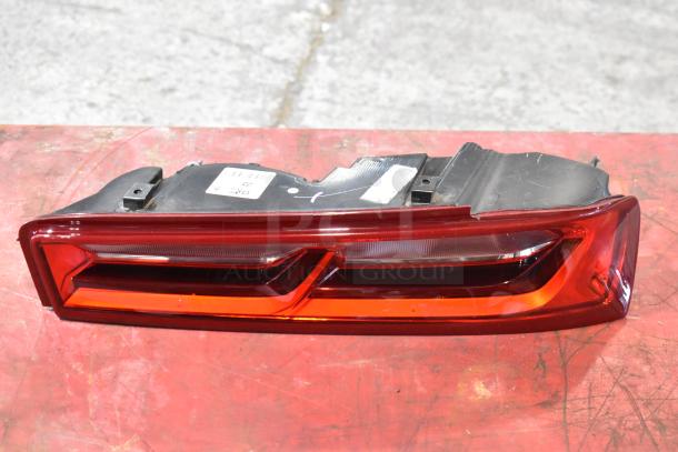 Red automotive brake light in used condition with visible label and mounting hardware on a red surface.
