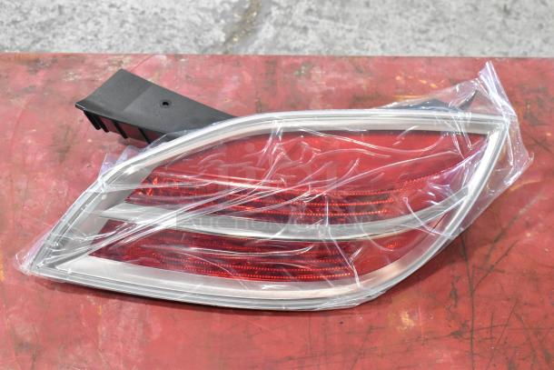 Plastic-wrapped car brake light with red lens and chrome trim resting on a red surface.