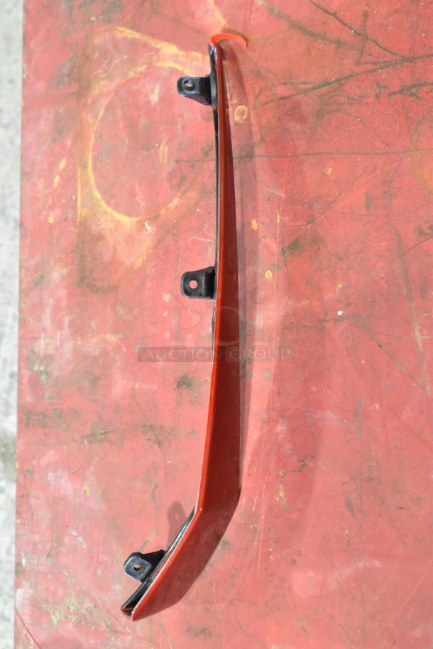 Red automotive trim piece with mounting brackets on a painted surface. Condition appears used.