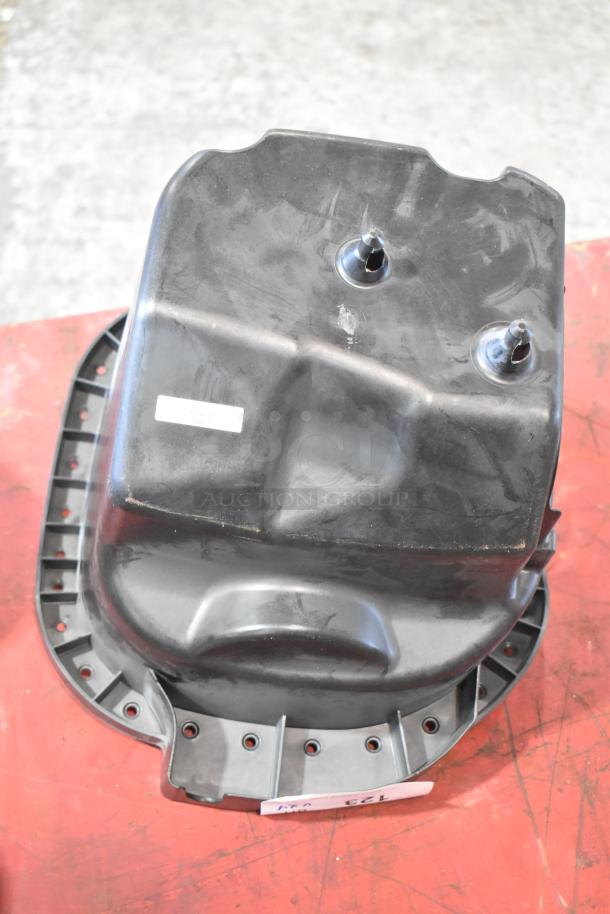 Plastic automotive part, black, possibly an oil pan, used condition, features multiple mounting holes and a small label.