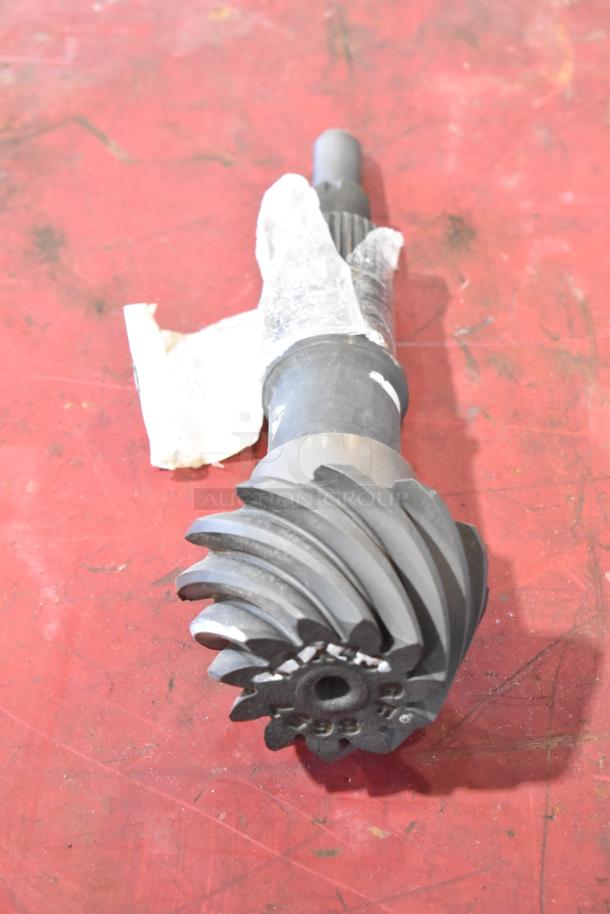 Car part with spiral gear and shaft, wrapped in clear plastic, placed on a red surface. Item in new condition.