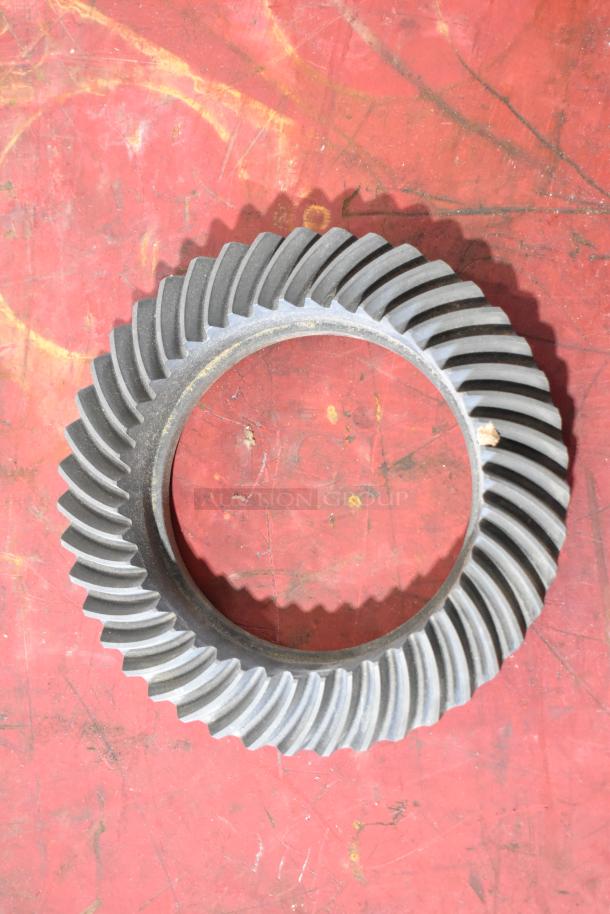 Round metal gear with spiral teeth on a red, worn surface. Appears in used condition. No visible labels or markings.