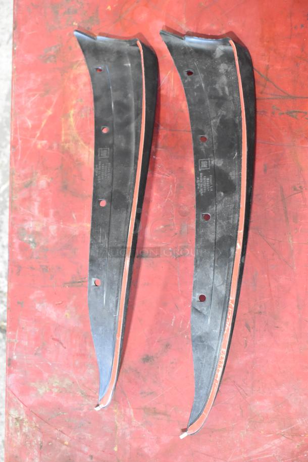 Two black curved plastic trims with red lining, showing mounting holes and manufacturer markings, used for automotive purposes.