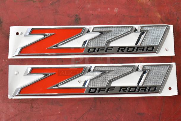 Two Z71 Off Road emblems, silver and red, pristine condition, mounted on white backing, six available for auction.