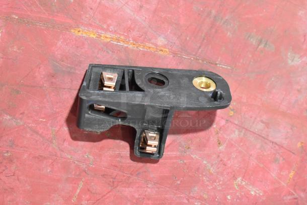 A black GM 22751230 door latch release switch, featuring copper connectors, in good condition on a red surface.