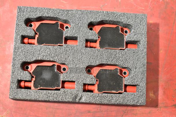 Lot of 4 red and black automotive ignition coils in foam packaging, showcasing good condition and uniform design.