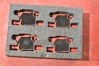 Lot of 4 red and black automotive ignition coils in foam packaging, showcasing good condition and uniform design.