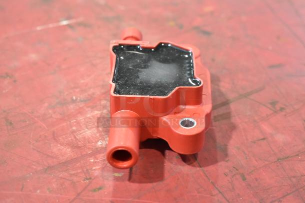 Red and black automotive ignition coil pack, slightly used, with visible wiring connectors and mounting holes.