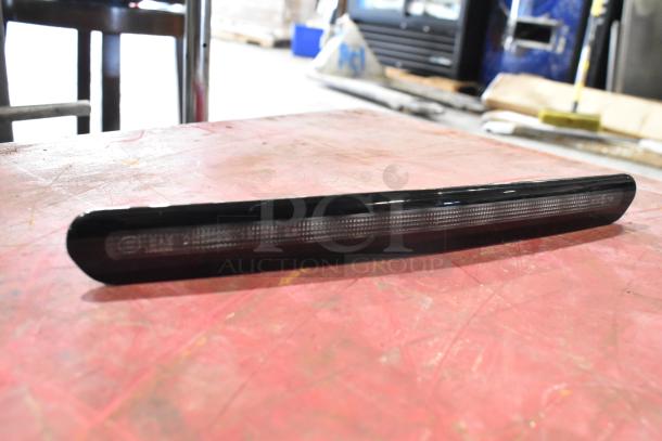 Black automotive part on a workbench, likely a switch or light component. Includes tags or markings for identification.